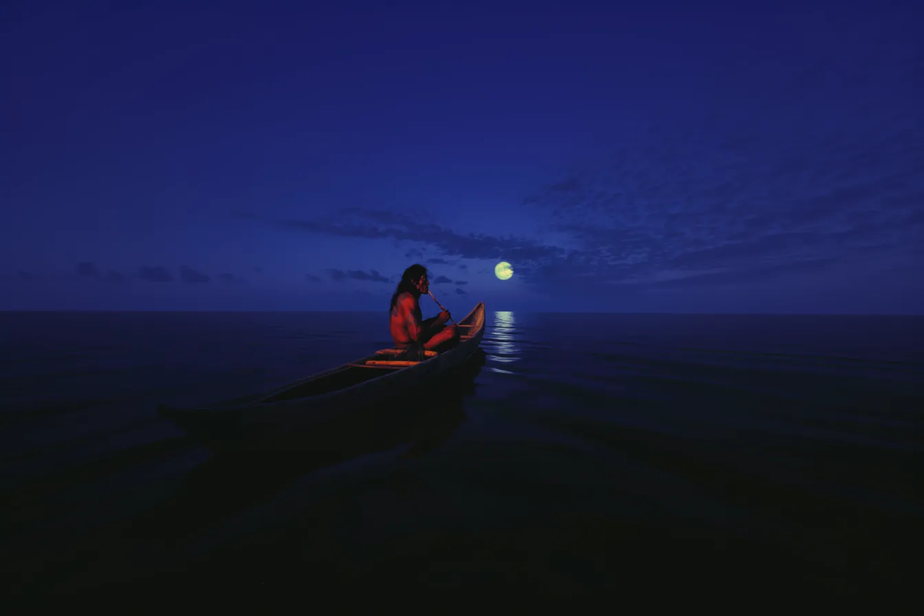Silueta de una persona sentada en una canoa de noche sobre un mar oscuro, iluminada por un resplandor cálido, con la luna llena reflejada en el agua.