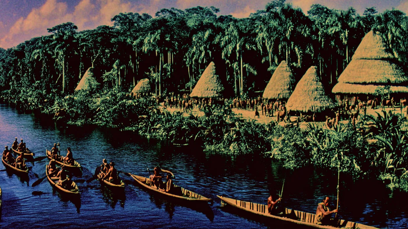 Aldea densa de chozas de techo de paja agrupadas junto a un río, con canoas de madera navegando entre ellas, rodeada de selva tropical bajo cielo despejado.