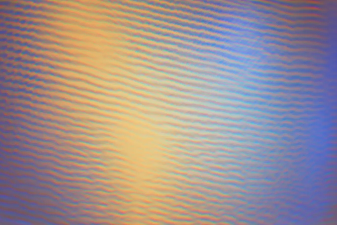 Textura abstracta de líneas onduladas diagonales, doradas y anaranjadas a la izquierda, azules a la derecha, con un brillo central luminoso.