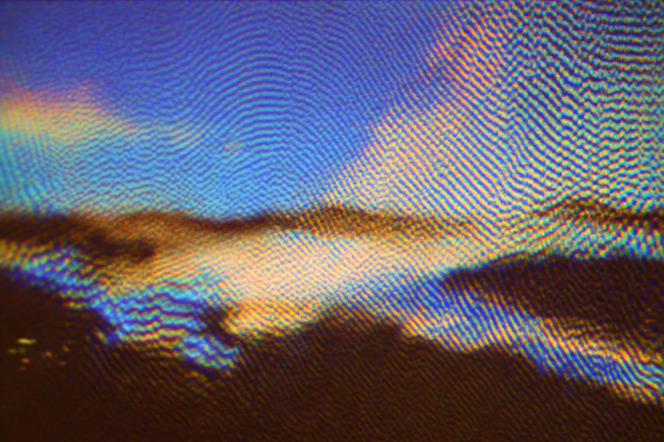 Textura abstracta con la silueta oscura de una cordillera en la parte inferior, cielo azul arriba y franjas de colores similares a un arcoíris cerca del horizonte.
