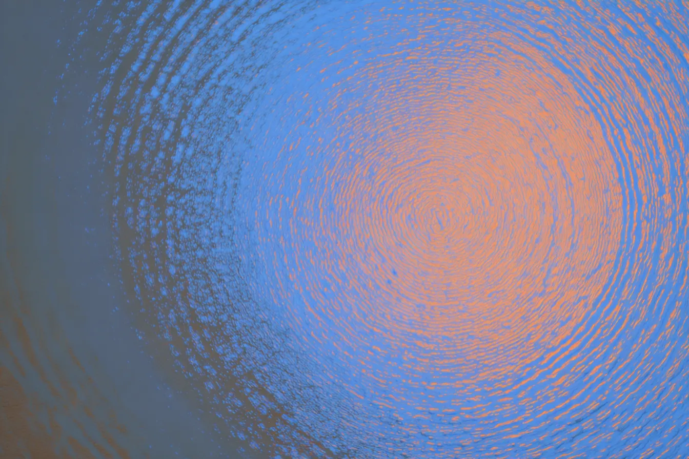 Textura abstracta de anillos concéntricos azules que rodean un resplandor central anaranjado y rosado.