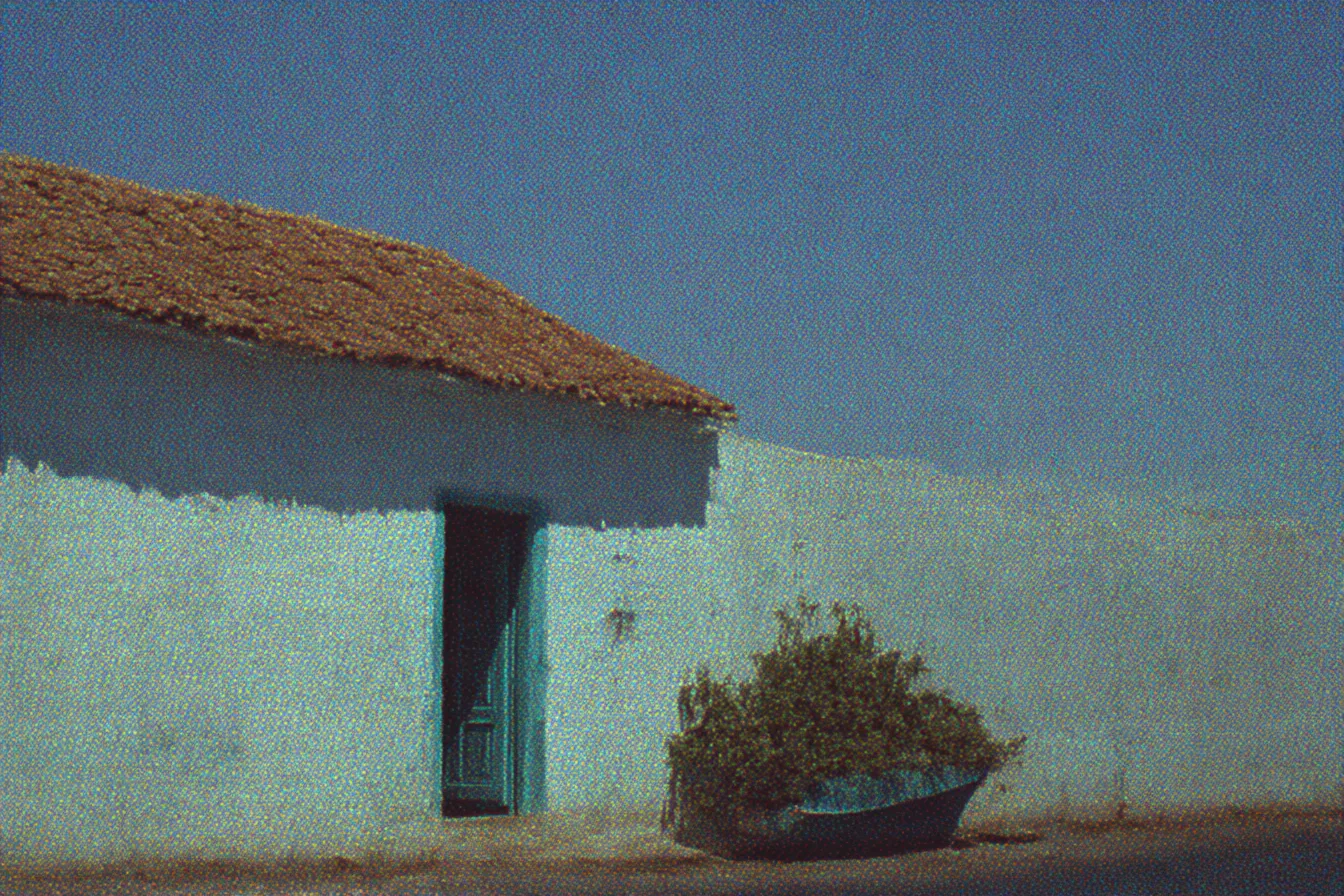 Casa de paredes turquesas con techo de paja y puerta azul, con un bote de madera lleno de arbustos apoyado en la fachada, bajo un cielo azul despejado.