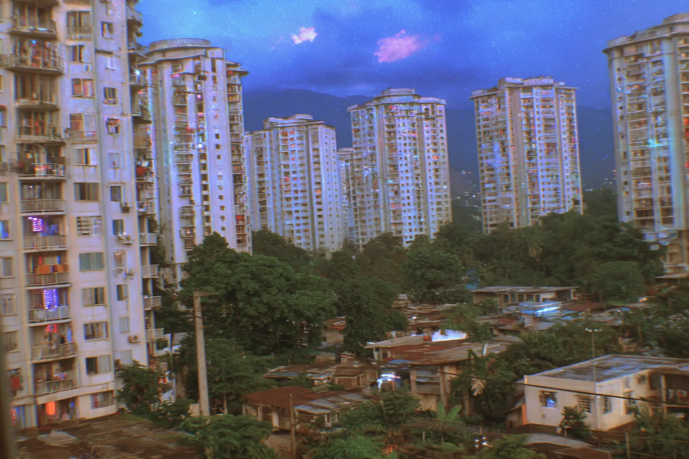 Fotografía de una ciudad al atardecer, con torres de apartamentos altas y un barrio de casas bajas en primer plano, bajo un cielo morado y azul.